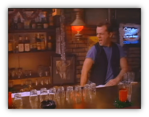 Bartender in a rustic bar with stacked glasses and colorful drink, expressing surprise.