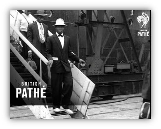 Black and white photo of a man in a suit and hat descending a staircase from a ship, with another person in the background.