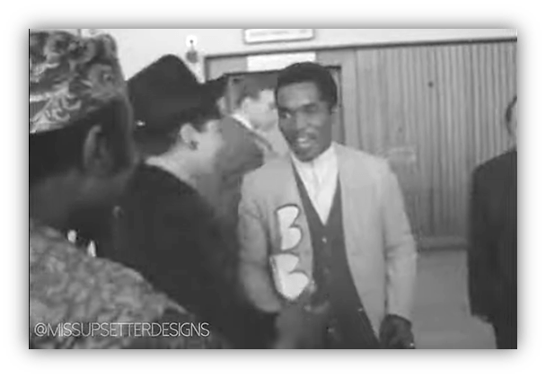 "Black and white image of a smiling man in a suit interacting with two others at a public event."