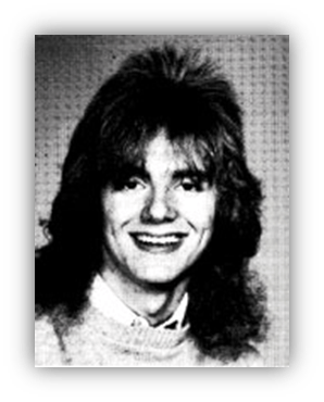 Young man with long, curly hair and a bright smile, wearing a light sweater.