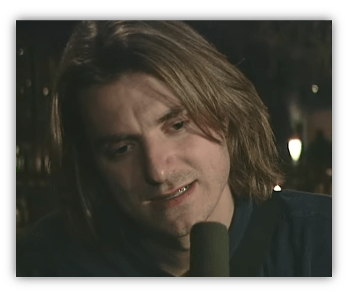 "Close-up of a man with long hair speaking into a microphone."