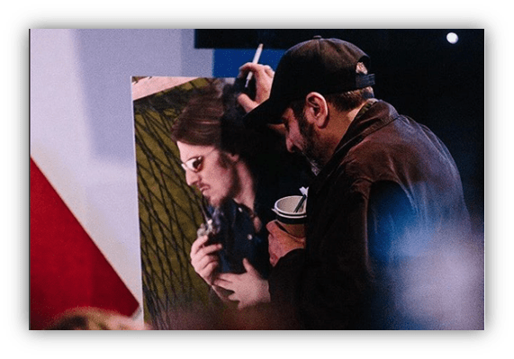 Artist painting a portrait of a man while holding a coffee cup.