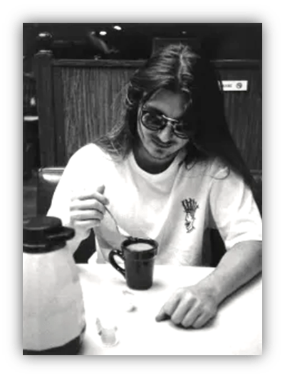 Young man in sunglasses stirring coffee at a diner table.