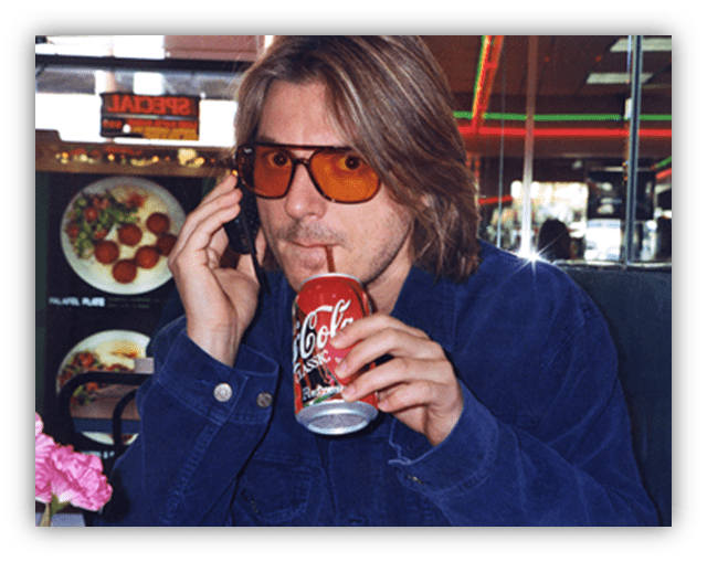Man in sunglasses talking on the phone while sipping from a Coca-Cola can in a diner setting.