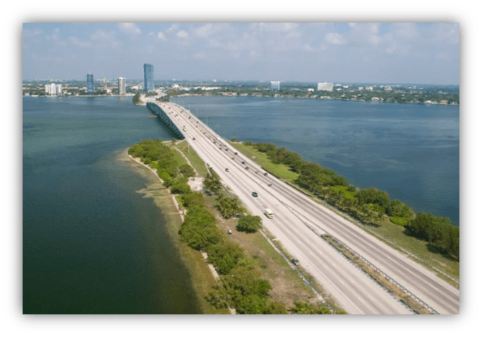 Aerial view of a highway bridge over water with city skyline in the background.