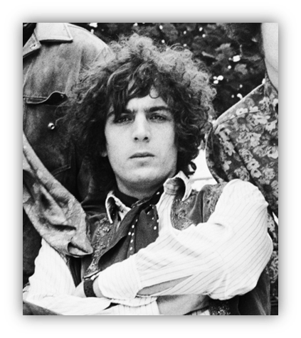 Black and white portrait of a young man with curly hair, wearing a vest and a striped shirt, sitting with arms crossed.