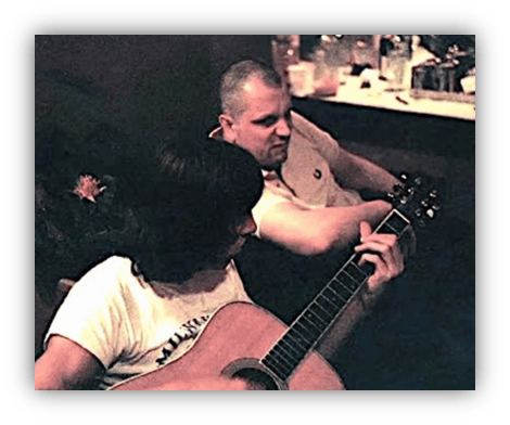 Two men relaxing and playing guitar together in a cozy setting.