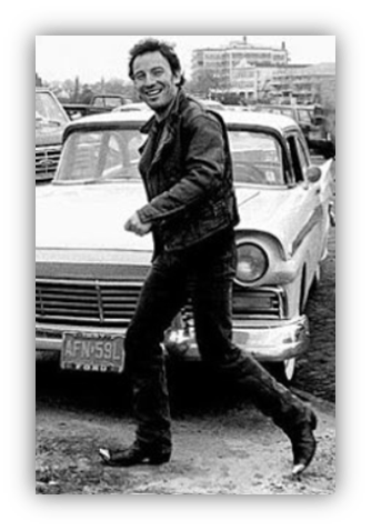 "Smiling man in a leather jacket walking by a vintage car."