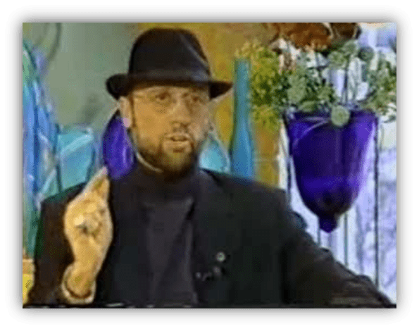 "Man in a black hat and glasses speaking during an interview, surrounded by colorful decor."