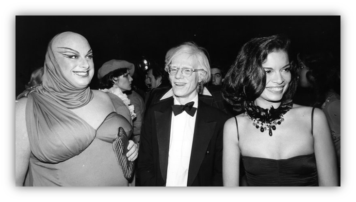"Black and white photo of three people at a glamorous event: a person in dramatic makeup, a man in a tuxedo, and a woman in an elegant dress."