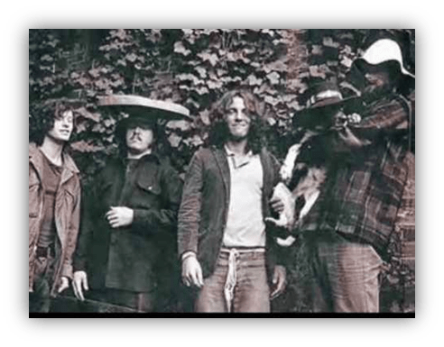 "Vintage photo of four musicians posing outdoors with a dog, surrounded by ivy."