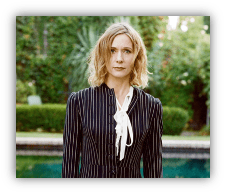 Woman in a striped dress standing by a pool surrounded by greenery.