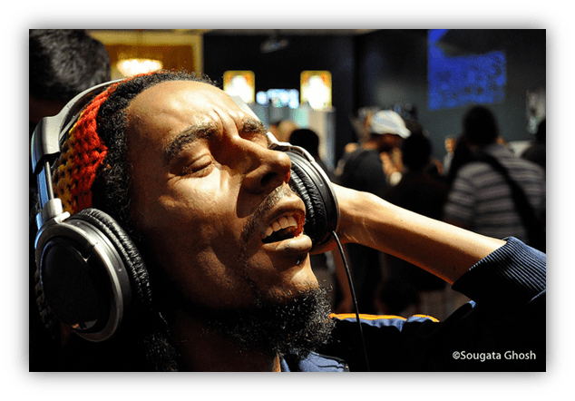 A man with dreadlocks enjoying music through headphones in a crowded setting.