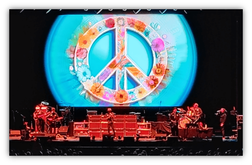 "Live band performance with a colorful peace symbol backdrop."