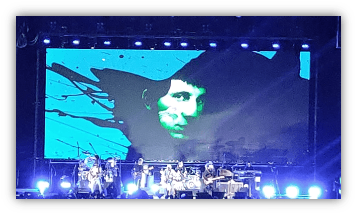 Concert scene featuring a band performing on stage with a vibrant blue and green backdrop.
