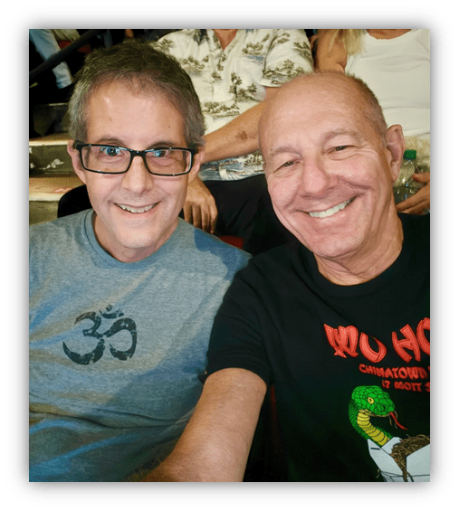 "Two friends smiling for a selfie at an event, with a lively crowd in the background."