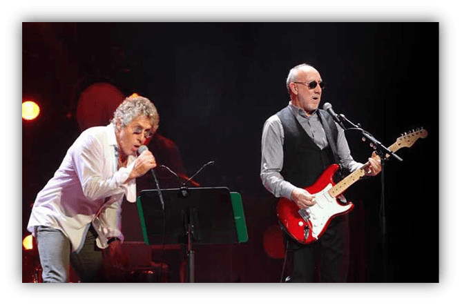 "Two musicians performing on stage, one singing and the other playing a red electric guitar."