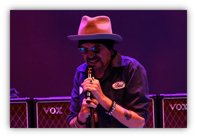 Singer performing on stage with microphone, surrounded by amplifiers.