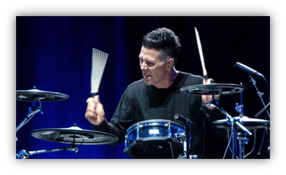 Drummer performing on stage with drumsticks and a lively expression.