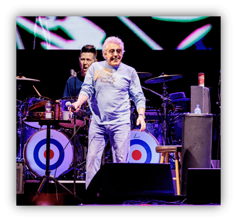"Live concert performance featuring a singer in a blue shirt with a drummer in the background."