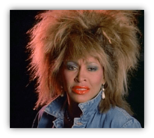 "Close-up of a woman with voluminous hair and bold makeup, wearing a denim jacket."