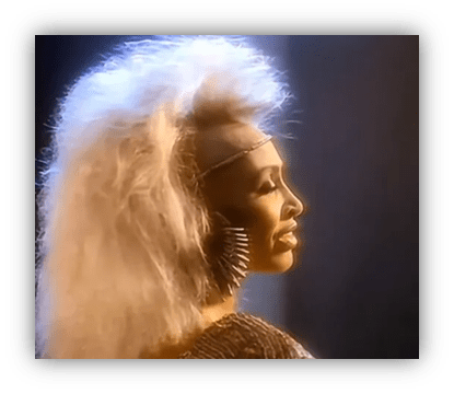 "Profile of a woman with voluminous hair and statement earrings, illuminated against a dark background."