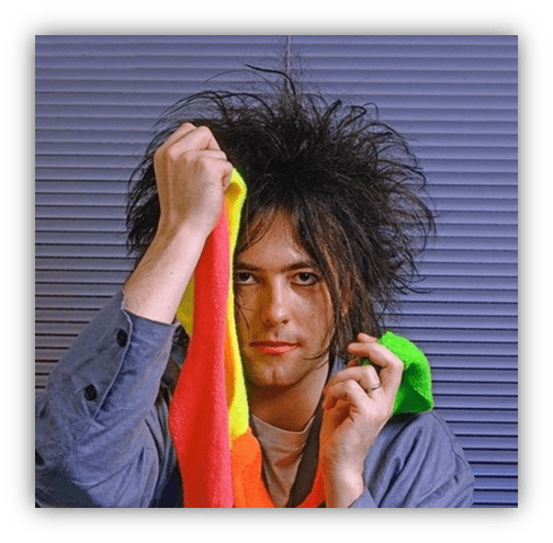 "Person with wild hair holding colorful towels against a textured backdrop."