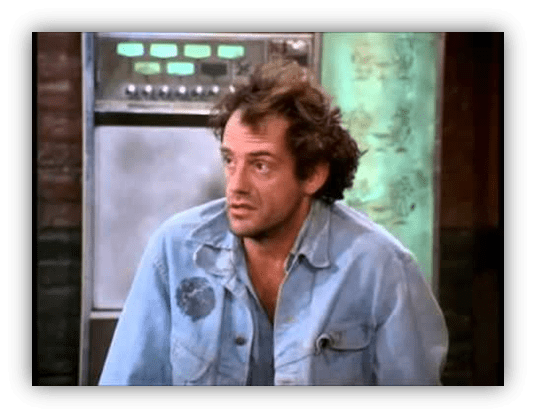 "Man in a denim jacket with tousled hair, sitting in a vintage setting."