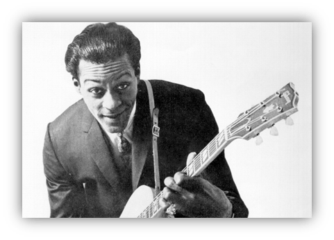 "Black and white photo of a smiling musician in a suit holding an electric guitar."