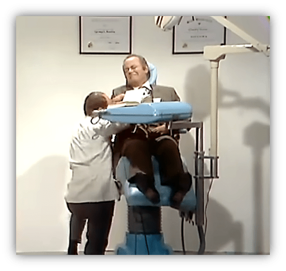 Man in a dental chair with a dentist preparing for treatment, dental certificates on the wall.