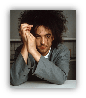 "Man with messy hair in a gray blazer, resting hands on a table."