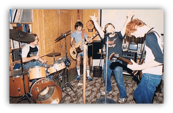 "Four musicians performing in a home setting, featuring drums, guitar, and vocals."