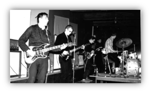 "Black and white photo of a band performing live on stage with guitars and drums."