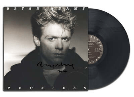 "Bryan Adams' 'Reckless' album cover with vinyl record, featuring a black-and-white portrait and signature."