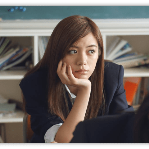 Student looking thoughtfully in a classroom with books in the background.