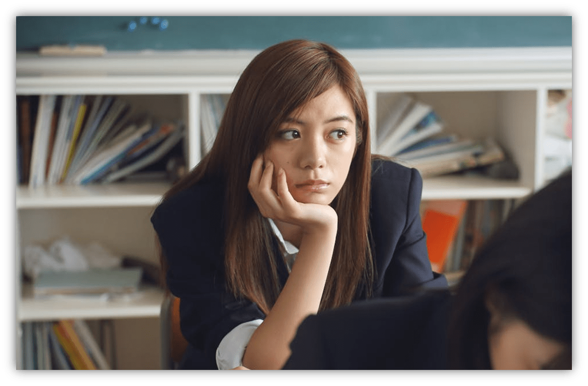 Student looking thoughtfully in a classroom with books in the background.