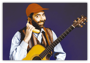 "Man in a cap holding a banana as a phone, smiling with an acoustic guitar."