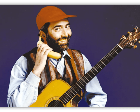 "Man in a cap holding a banana as a phone, smiling with an acoustic guitar."