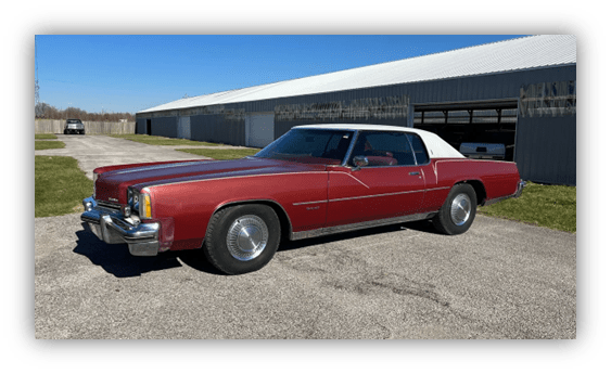 Classic red car with a white vinyl top parked on a sunny day.