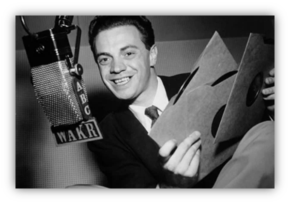 Vintage radio host smiling with vinyl records at WAKR microphone.
