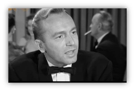 Classic black and white image of a man in a tuxedo, engaged in conversation at a social event.