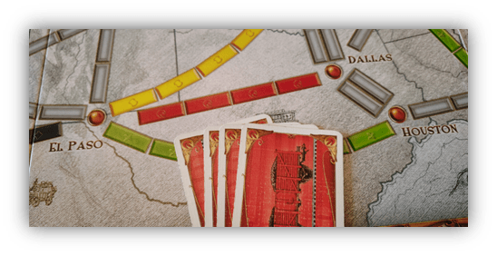 "Close-up of a board game with train routes and playing cards featuring a locomotive design."