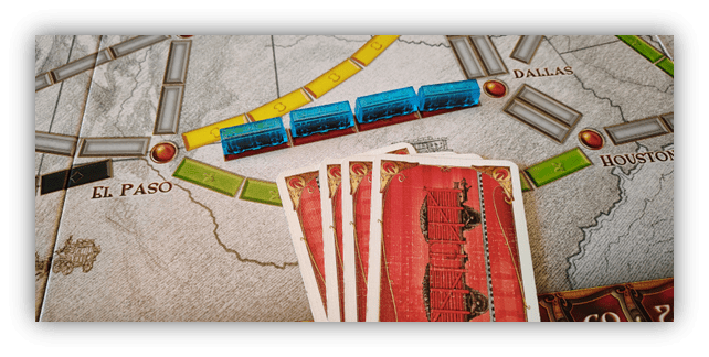 "Close-up of a board game featuring colorful train pieces and playing cards on a map."