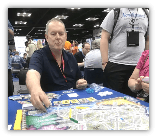 "Man playing a board game at a gaming convention, surrounded by other attendees."