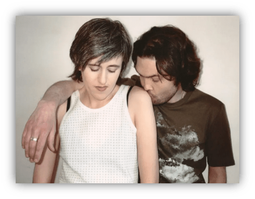 "Intimate portrait of a couple, with the man leaning in towards the woman's shoulder."