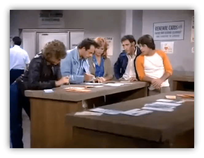 Group of people filling out forms at a counter in a government office setting.