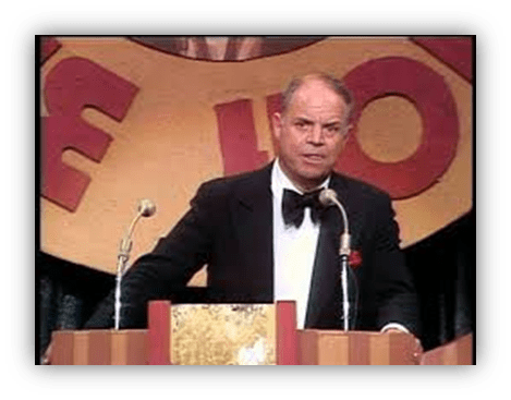 "Don Rickles performing at a comedy event, standing at a podium with microphones."