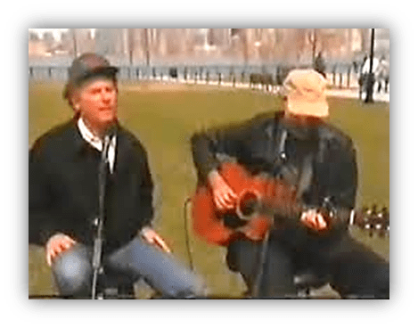 "Two musicians performing live outdoors with a guitar in a park setting."