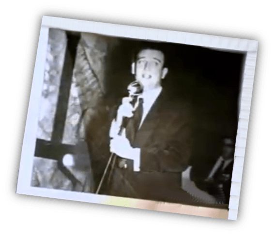 Black and white photo of a man singing into a microphone on stage.