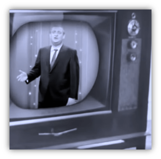 Man in a suit speaking on a vintage television set.
